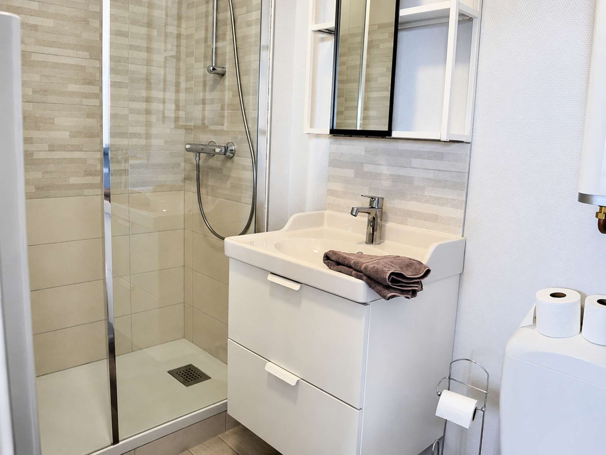 A modern bathroom with a glass-enclosed shower, a white sink with a towel, and a toilet paper holder.
