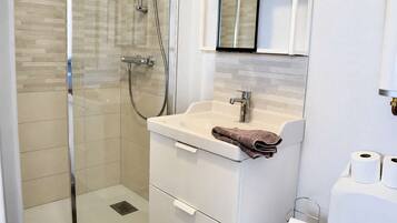 A modern bathroom with a glass-enclosed shower, a white sink with a towel, and a toilet paper holder.