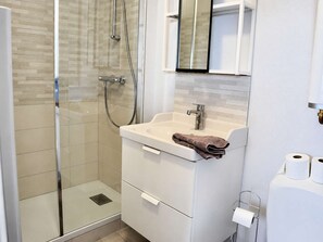 A modern bathroom with a glass-enclosed shower, a white sink with a towel, and a toilet paper holder.