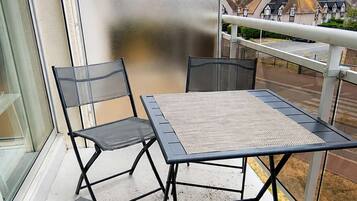 Un balcon avec une table et des chaises, une porte en verre dépoli et une vue sur les maisons au loin.