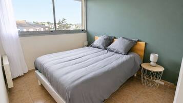 Une chambre à coucher avec un lit, une table de chevet, une lampe et une vue sur l’extérieur.