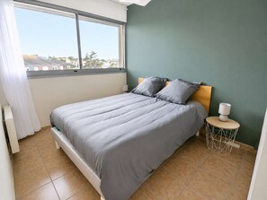 A bedroom with a bed, a bedside table, a lamp, and a view of the outside.
