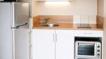 A compact kitchen with white cabinets, a stainless steel refrigerator, a built-in oven, and a microwave.