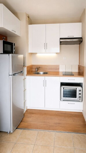 A compact kitchen with white cabinets, a stainless steel refrigerator, a built-in oven, and a microwave. - Bienvenue chez nous ! (Courseulles-sur-Mer)