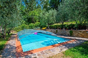 Piscina com cobertura de vidro, cercada por paredes de pedra e vegetação exuberante.