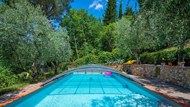Una piscina exterior rodeada de árboles y muros de piedra.