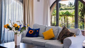 Una sala de estar con un sofá gris, un jarrón con flores y vistas a la vegetación a través de un ventanal amplio.