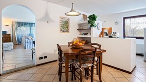 Un comedor con mesa y sillas de madera, una lámpara colgante y una encimera de cocina con varios objetos.