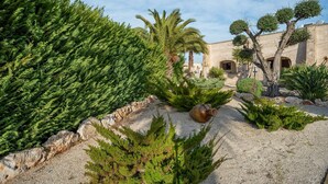 Ein Garten mit verschiedenen Pflanzen, einer Steinmauer und einem Gebäude mit Bögen.