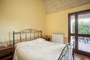 Ein Schlafzimmer mit einem Bett, einem Nachttisch, einem Heizkörper und einer Glastür, die zu einem Außenbereich führt.
