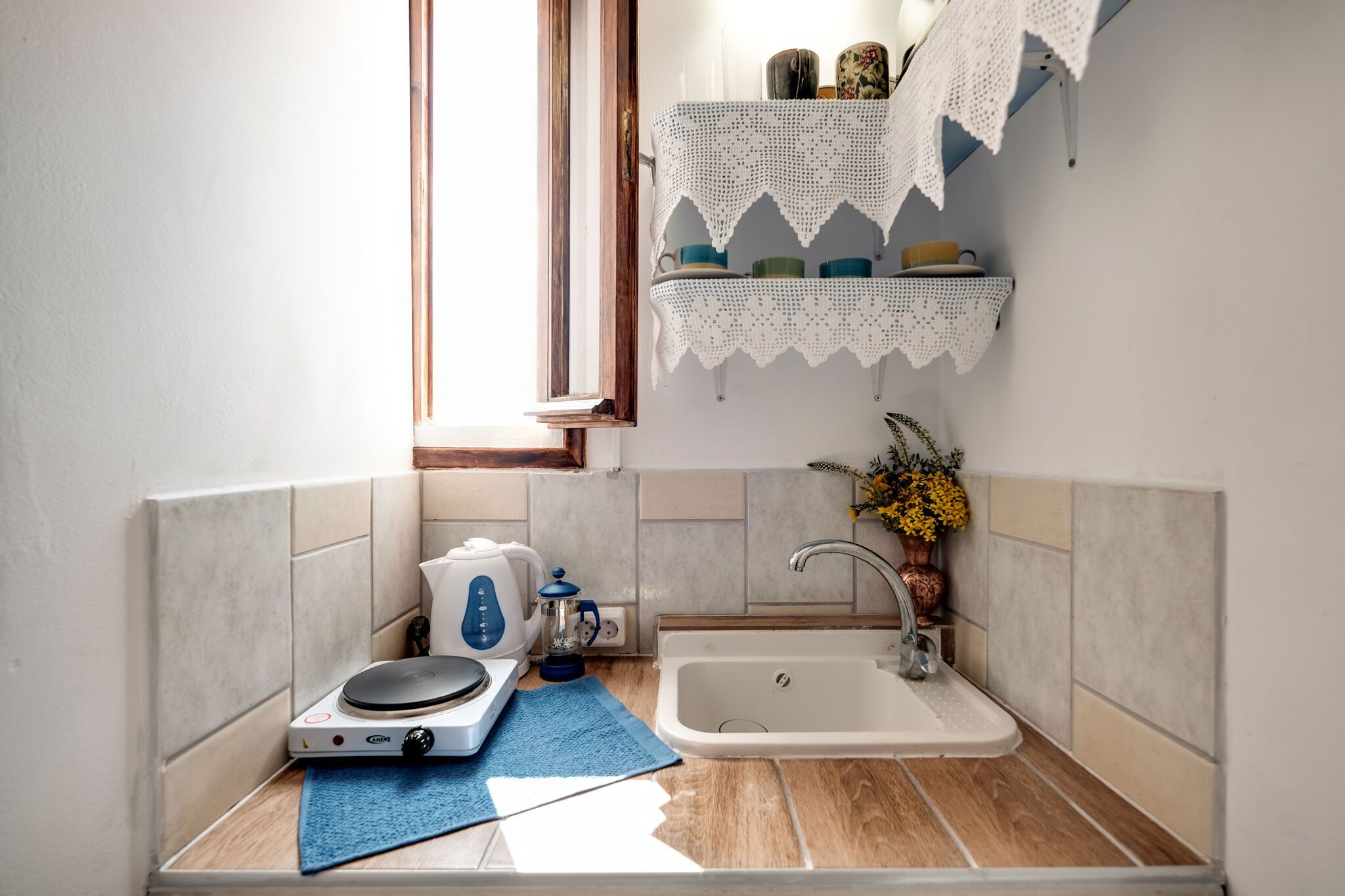 Una pequeña cocina con hervidor, cafetera, lavabo y ventana.