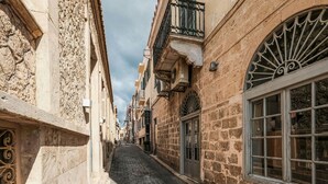 A narrow cobblestone street flanked by historic stone buildings with ornate balconies and large windows. - Holiday Home in Aegina Island (Aegina Island)