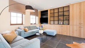 Una sala de estar moderna con un sofá seccional, una mesa redonda de centro y un mueble grande de madera con puertas de vidrio.