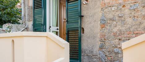 A narrow alleyway with a beige wall and a brick wall with a wooden door and green shutters.