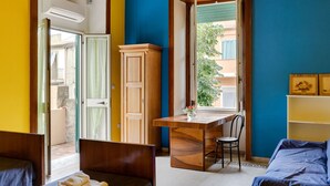 Une pièce comprenant un lit, un bureau et une chaise. Il y a une fenêtre donnant sur les bâtiments à l’extérieur.
