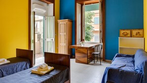 Une chambre avec deux lits, un bureau en bois, une chaise et une petite table sur laquelle se trouve un vase.