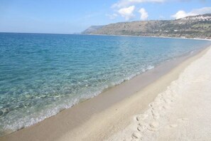 A beach with clear water, a sandy shore, and a hilly landscape in the background.