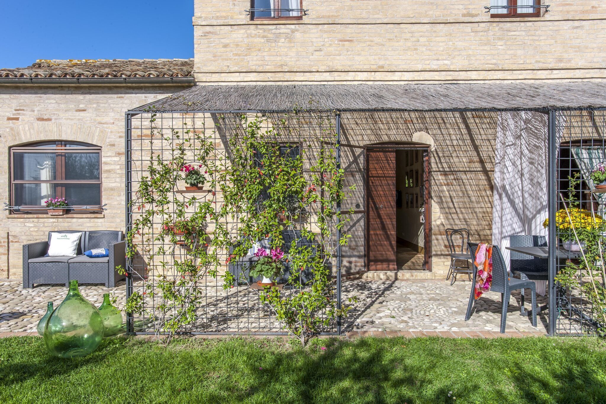 A courtyard with a pergola, outdoor seating, and a stone building.