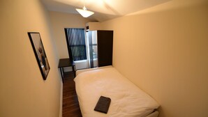 Un dormitorio con cama, un cuadro en la pared, una ventana con persianas y un radiador.