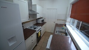 Cocina compacta con armarios blancos, estufa a gas, microondas y pileta.