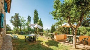 Eine Terrass mit Tischen und Stühlen, umgeben von Bäumen und einer Steinmauer.