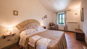 Ein Schlafzimmer mit einem großen Bett, Nachttischlampen, einem Sessel, einem Fenster mit Vorhängen und einer Heizung.