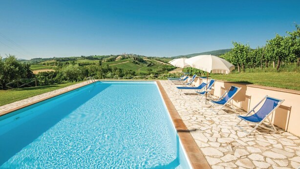 A swimming pool with blue water, surrounded by stone tiles and blue lounge chairs.