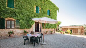 A building covered in green ivy, a gravel patio with a table and chairs, and potted plants.