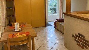 A small, cozy room with a wooden table and chairs, a sofa, and a sliding door leading to a balcony.