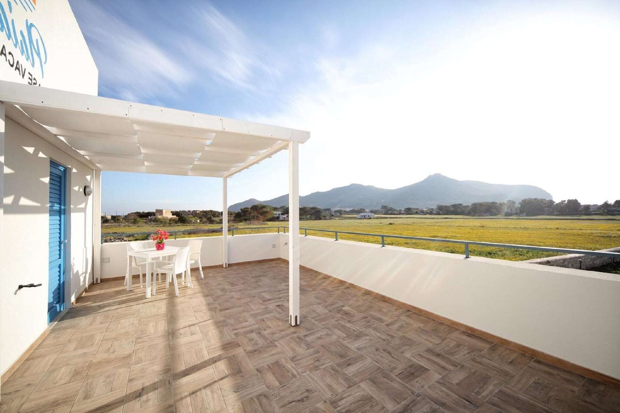 A covered outdoor area with a table and chairs, a white door, and a view of a field and mountains.