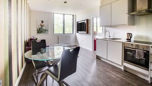 A modern kitchen with a glass dining table, stainless steel appliances, and a large window providing natural light.