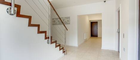 Un interior moderno con una escalera, un pasillo y una puerta al final.