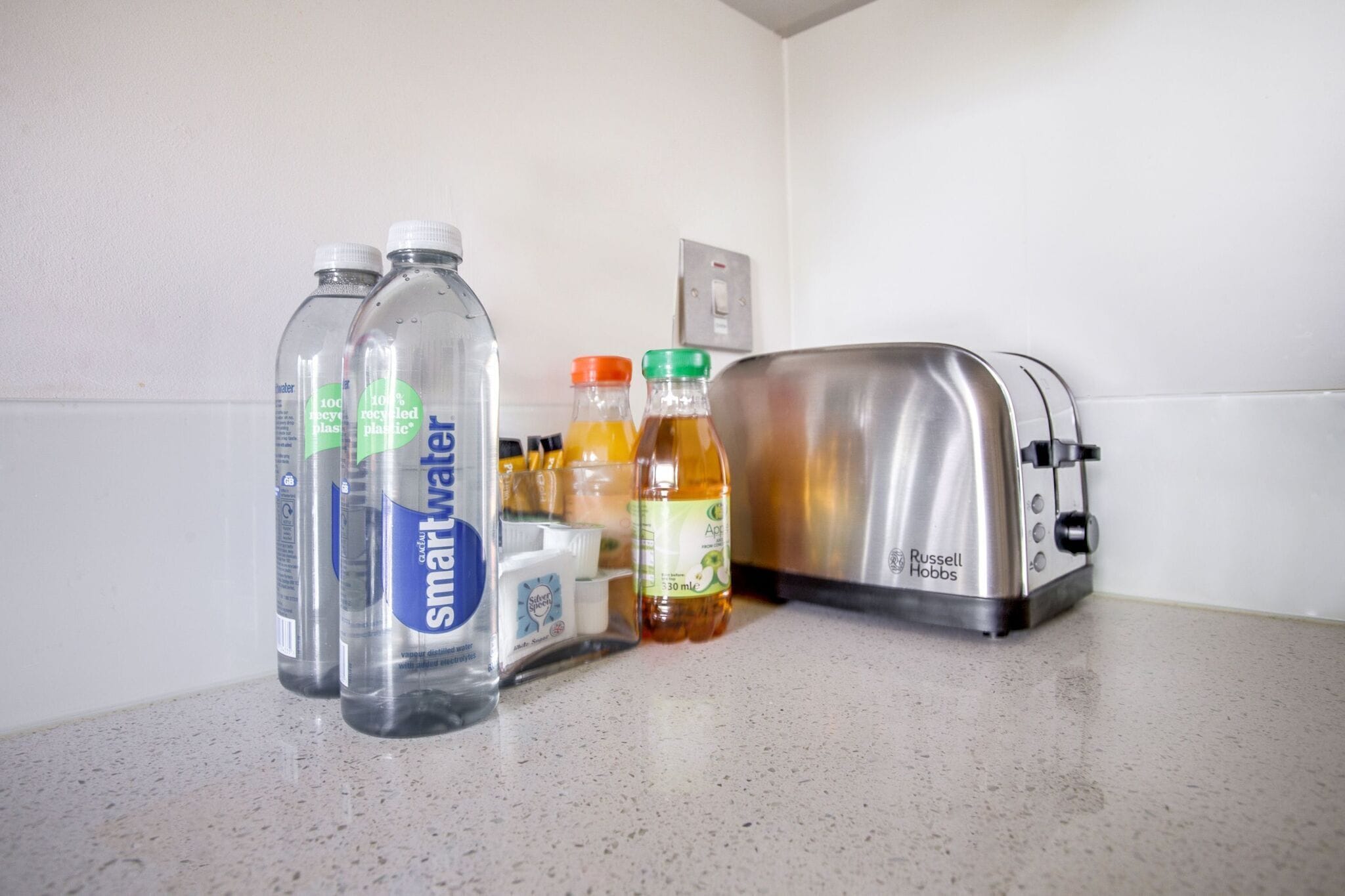 Eine Küchenarbeitsplatte mit einem Toaster, Smartwater-Flaschen und weiteren Getränken.