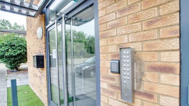A modern building entrance with a glass door and a keypad entry system.