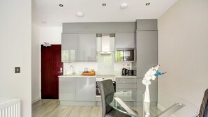 Une cuisine moderne avec des meubles gris, une table à manger en verre et une porte rouge.