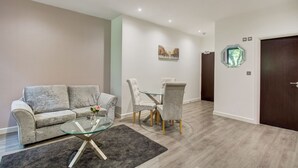 Een moderne woonkamer met een grijze bank, een glazen salontafel en een eethoek met een glazen tafel en stoelen.