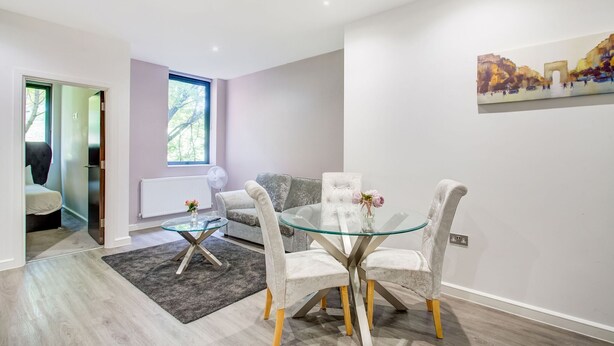 Een moderne woonkamer met een glazen eettafel, grijze fauteuils, een grijze bank en een groot raam.