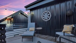 En udendørs siddeplads med to loungesæder, et rundt sofabord og en dekorativ vægdekoration.