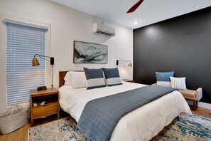 Une chambre moderne avec un grand lit, des tables de chevet, un climatiseur fixé au mur et un tableau.