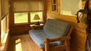 A cozy cabin room with a wooden floor, a patterned sofa, a map on the wall, and a window with a view of the outdoors.