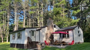 A cabin with a stone chimney, a porch with steps, and a red umbrella.
