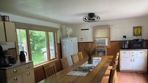A kitchen with a wooden table, chairs, a refrigerator, a microwave, and a ceiling fan.
