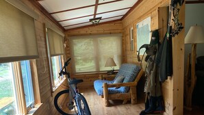 A wooden cabin interior with a bicycle, a blue cushioned chair, a lamp, and a hat on a bench.