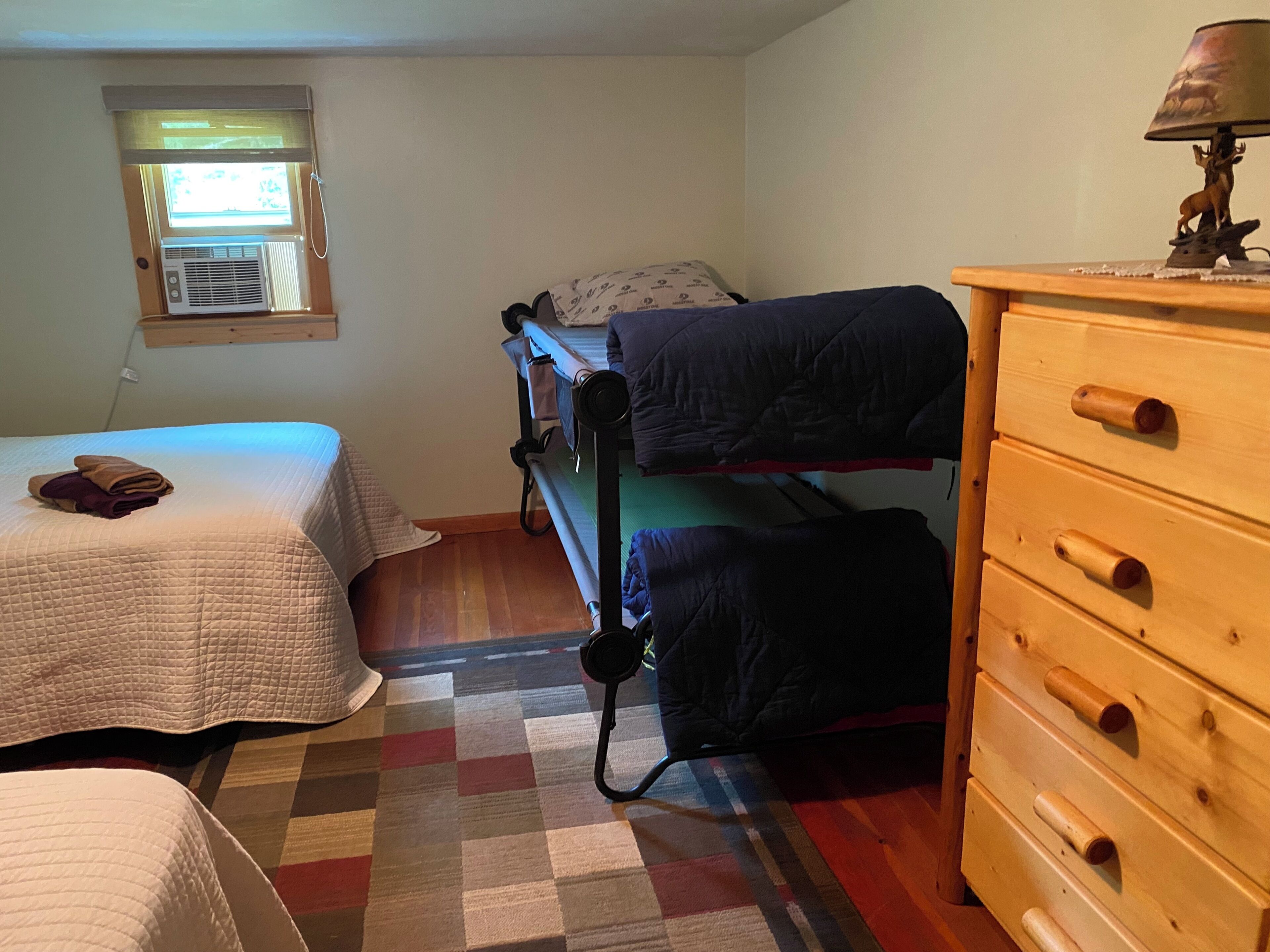 A bedroom with two beds, a wooden dresser, and a window with blinds.