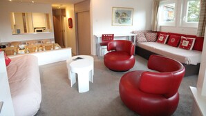 Een moderne woonkamer met een bank, rode stoelen, een witte salontafel en een eethoek met een tafel en stoelen.