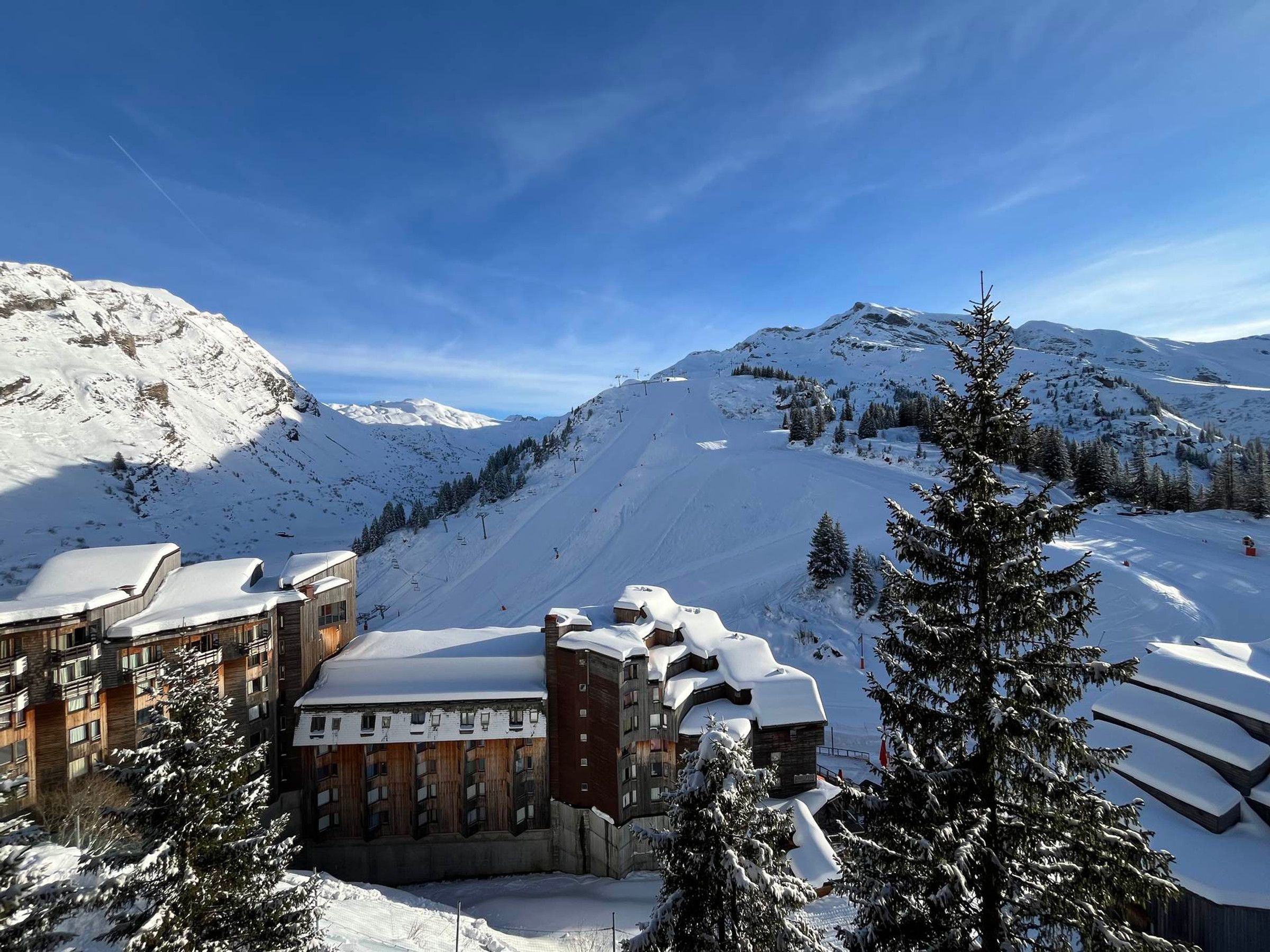 Un complejo turístico en la montaña cubierto de nieve, con un telesilla, edificios de madera y árboles nevados.