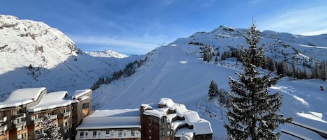 Un complejo turístico en la montaña cubierto de nieve, con un telesilla, edificios de madera y árboles nevados.