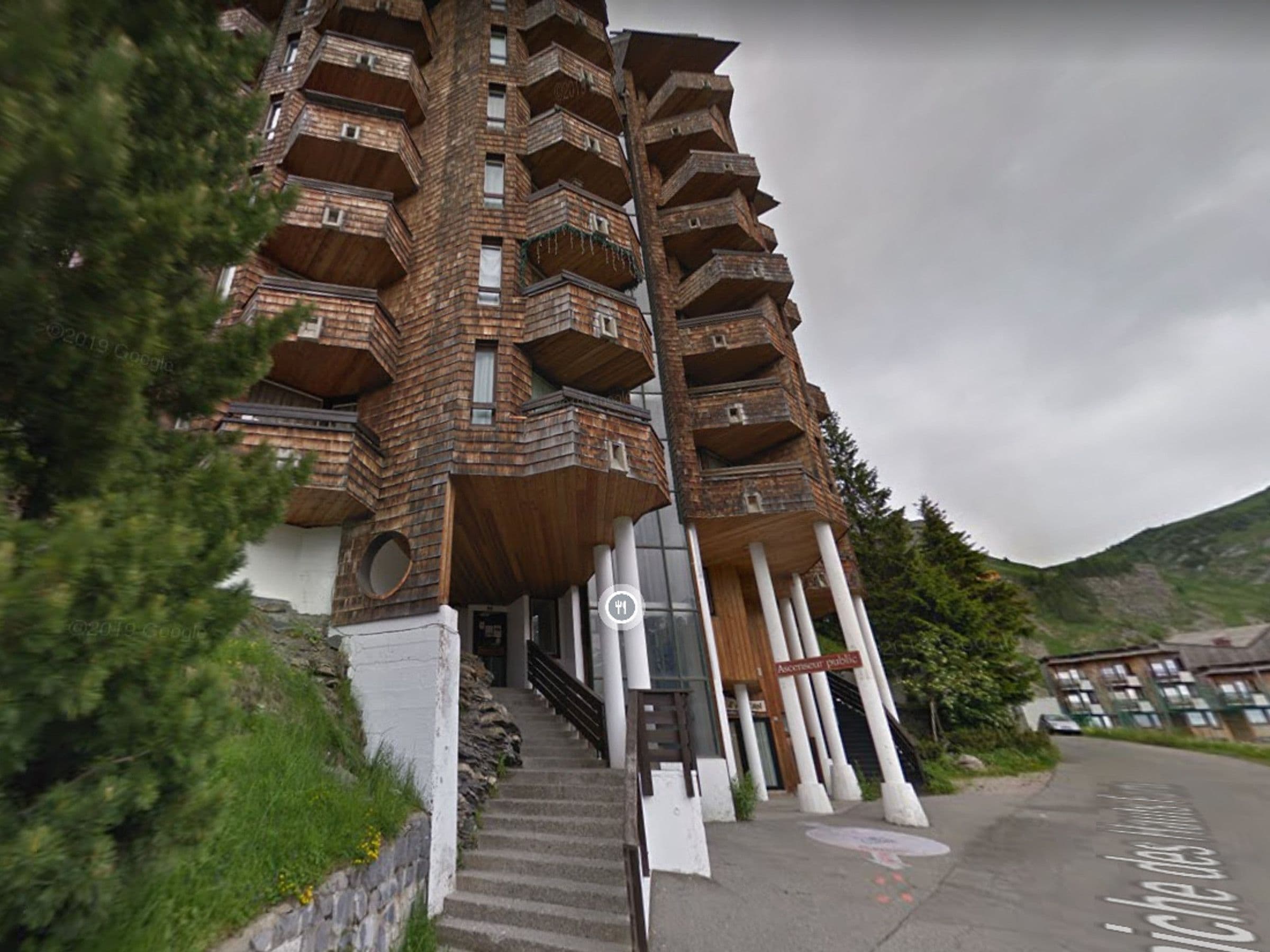 A multi-story building with a unique architectural design, featuring balconies and a staircase leading to the entrance.