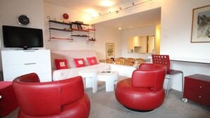 Een moderne woonkamer met een bank, rode stoelen, een televisie en een eethoek.