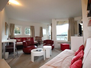 En stue med en sofa, røde stole, et lille hvidt bord og et fjernsyn.